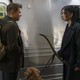 Clint and Kate look at each other while standing on a subway platform. Clint wears a backpack and Kate holds a bow.