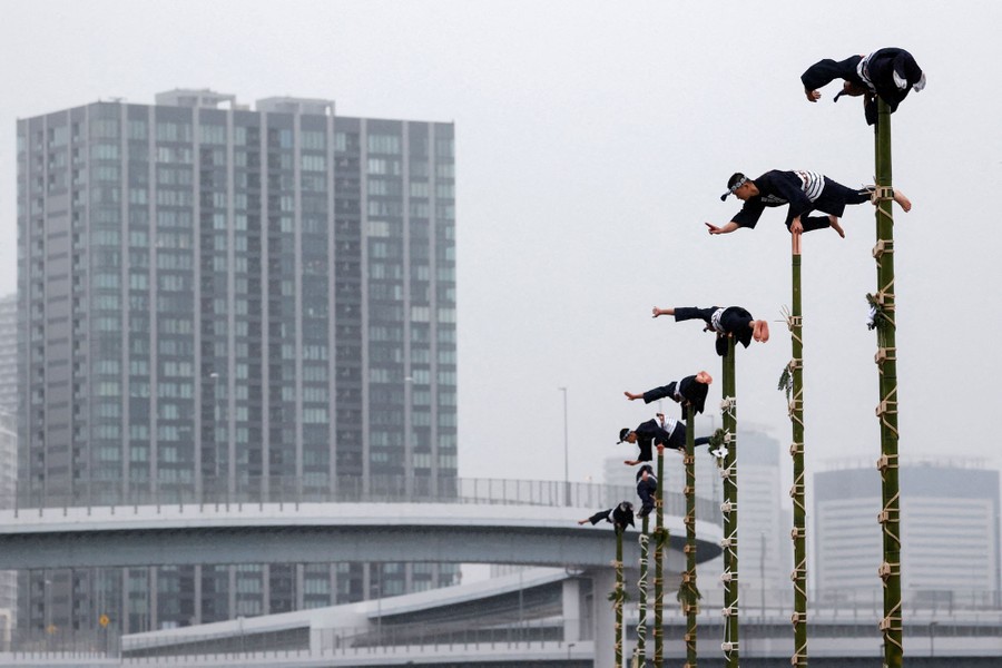 Men in traditional clothing balance atop high poles.