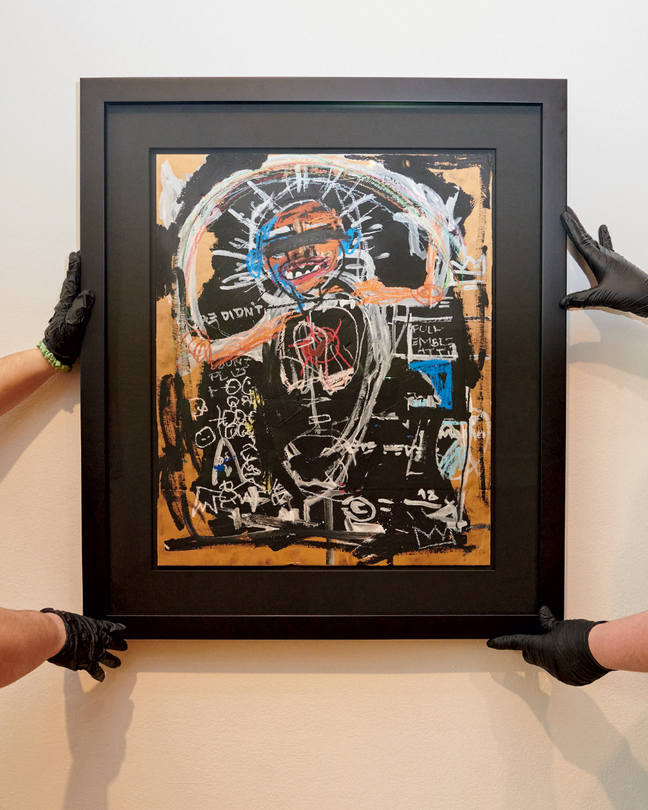 Four gloved hands mounting an allegedly forged Basquiat painting to a wall
