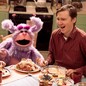 two people sitting at dinner table laughing next to a purple puppet