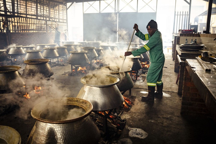 Ένα άτομο ανακατεύει μια από τις δεκάδες μεγάλες κατσαρόλες με φαγητό, μαγειρεύοντας πάνω σε ανοιχτές εστίες.