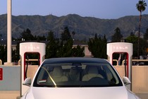 A photograph of a white Tesla between two superchargers.