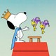 Atop his doghouse, Snoopy wears a crown and a cape as two small yellow birds in jester costumes hover.