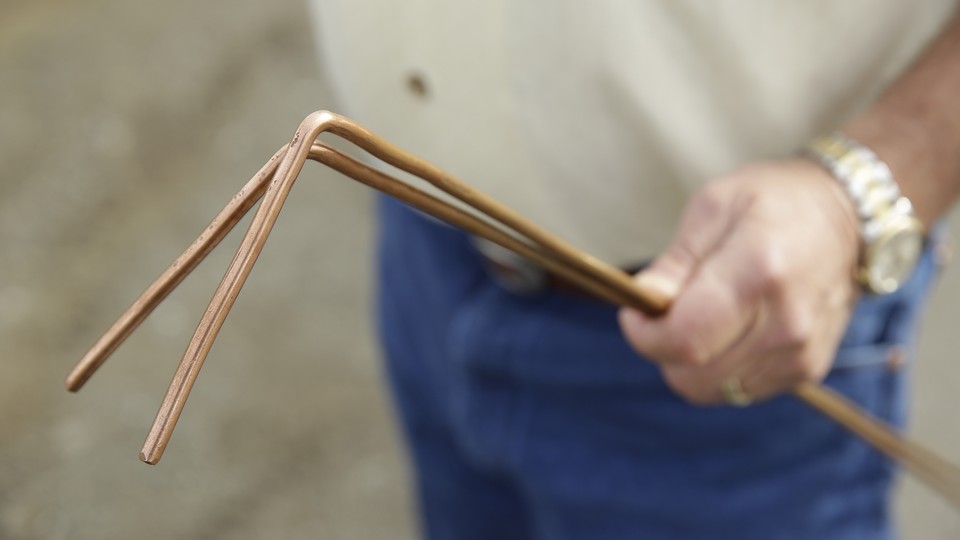 A water witch holds a pair of copper divining rods.