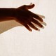 a hand outstretched in front of a white curtain, its shadow beneath it