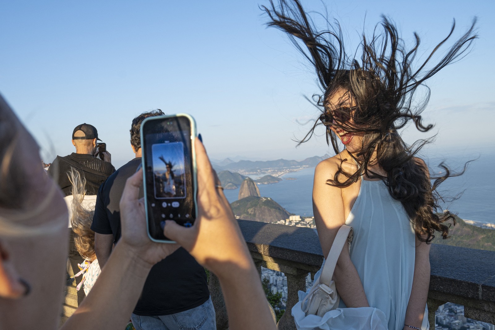 A tourist poses for a photograph overlooking Rio de Janeiro, as the wind blows their long hair upward.