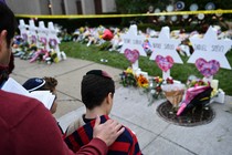 A man places his hand on the back of a boy while standing in front of a memorial.