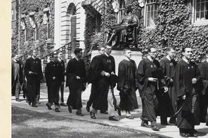 A black and white photograph of male Harvard students from the 1950s in graduation robes processing past an ivy-lined building and the John Harvard statue