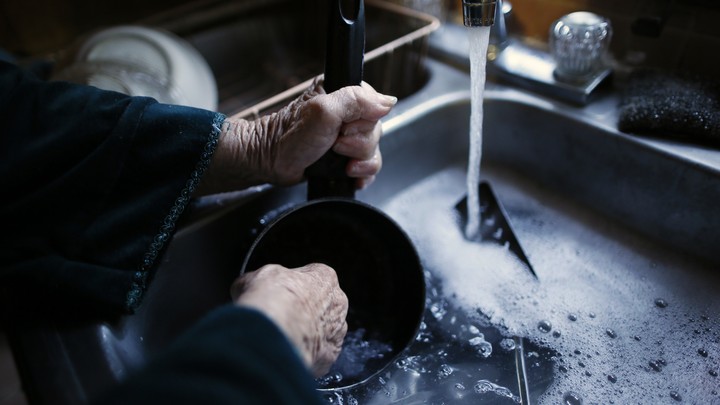 An elderly woman's hands washing a pot in a sink