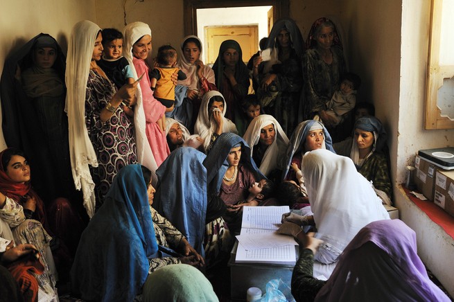 Women packed tightly together listen to a woman talk in a small room.