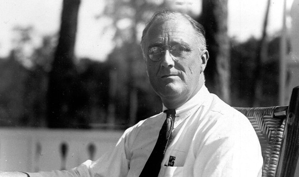 A black-and-white photo of Franklin D. Roosevelt, sitting in a chair and looking at the camera