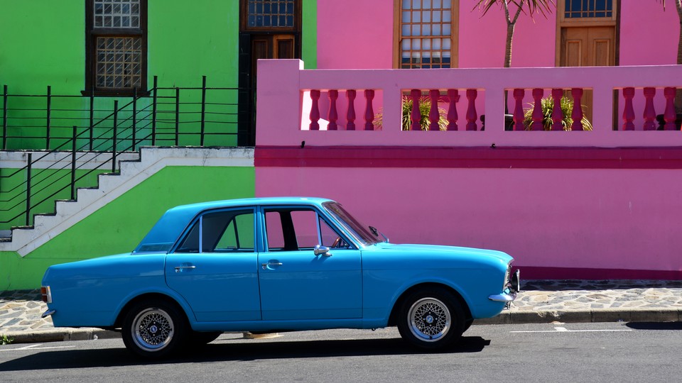 A bright blue car parked in front of pastel pink and green buildings