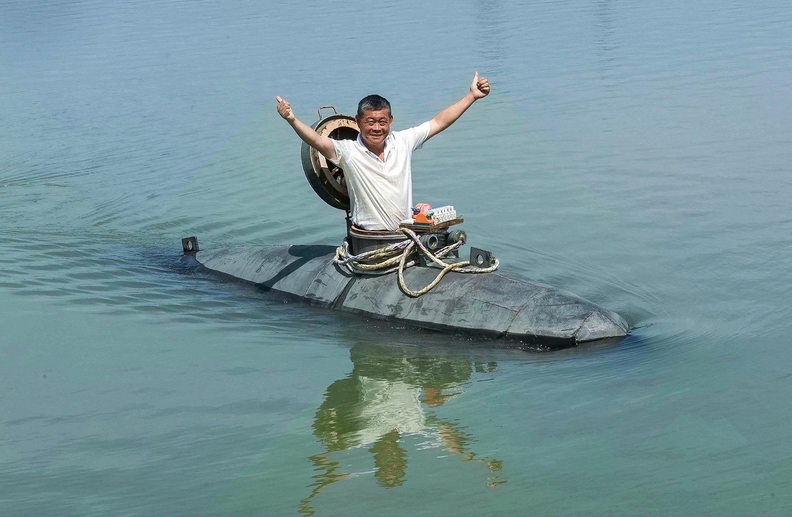A man poses, arms up, in the opening of a small submarine floating past.