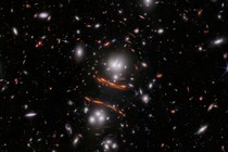 A view of many galaxies in deep space, with several of them smeared, distorted, and magnified in the center