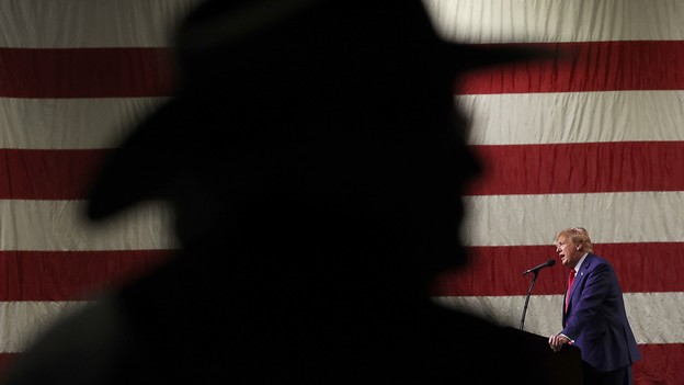 Trump speaking in front of a shadow over the American flag