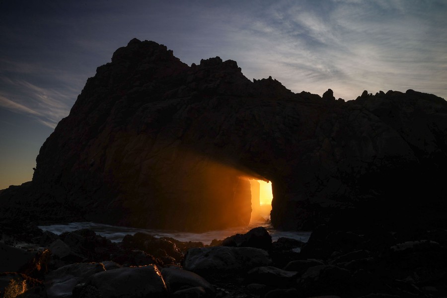Sunlight passes through a natural arch on a seashore.