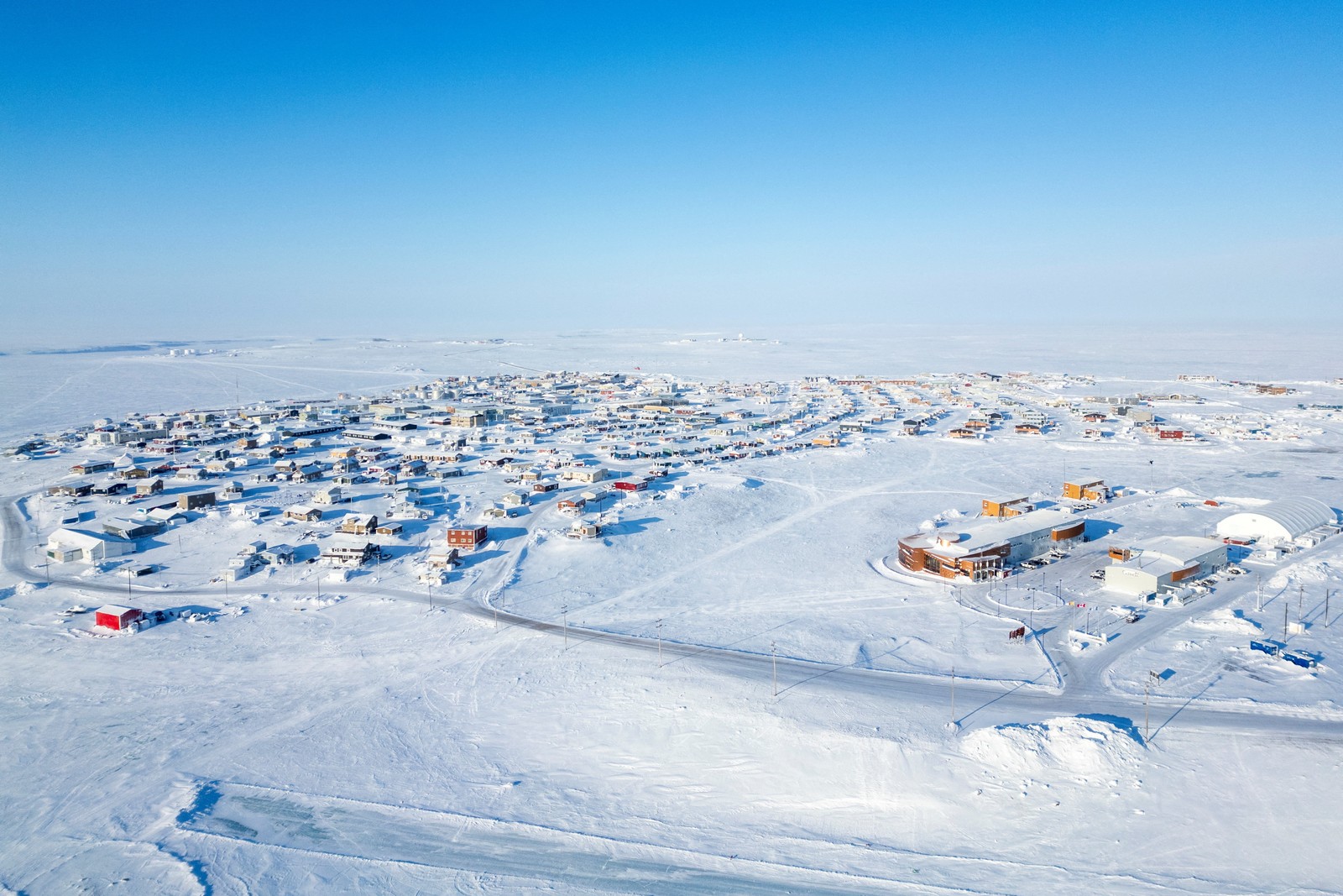 A drone view of an Arctic village in winter, with a broad snow-covered horizon in the background