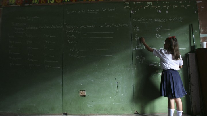 A child writes on a large chalkboard. Half the image is in shadows.
