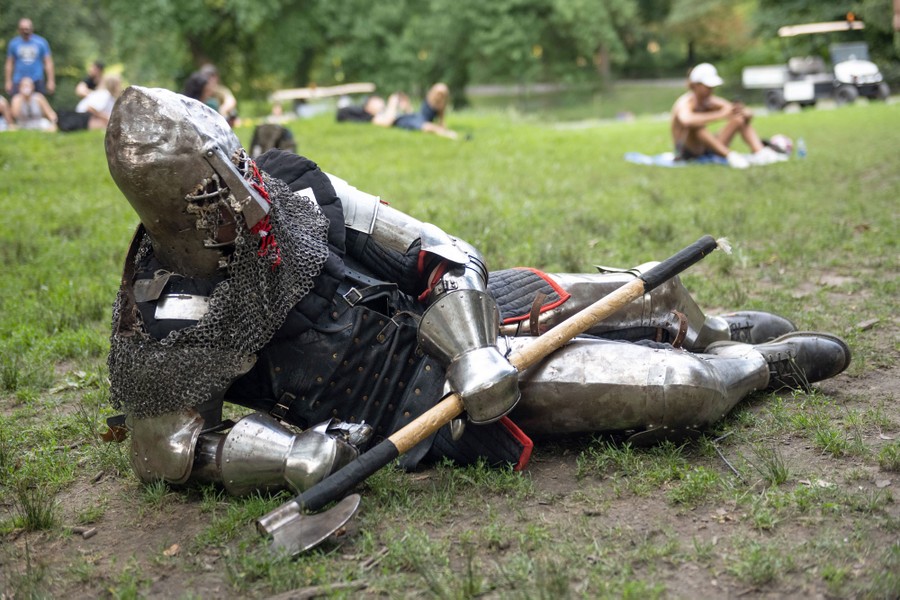 A person dressed in medieval armor lies down in a park.