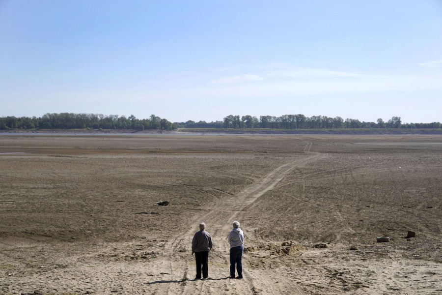People look out over a dry area where the normally wide Mississippi River has been reduced to a narrow trickle off in the distance