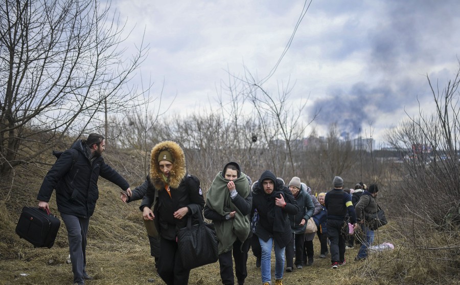 People fleeing a war zone walk through a field.