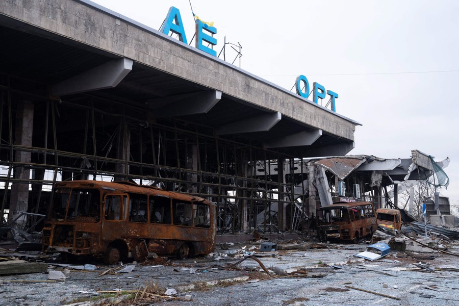 Rusted buses sit wrecked in front of the ruined facade of an airport terminal.