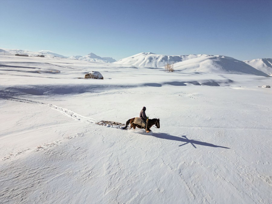 A person rides a horse through deep snow in a wide, open field.