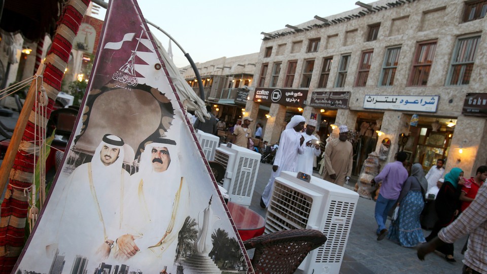 People walk past a banner bearing portraits of Qatar's former emir, Sheikh Hamad bin Khalifa al-Thani, and his son Sheikh Tamim.