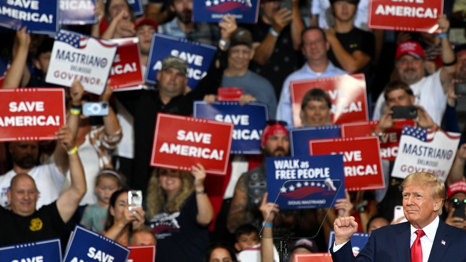 Donald Trump raises a fist, a crowd of supporters holding "save America!" signs stand behind him.