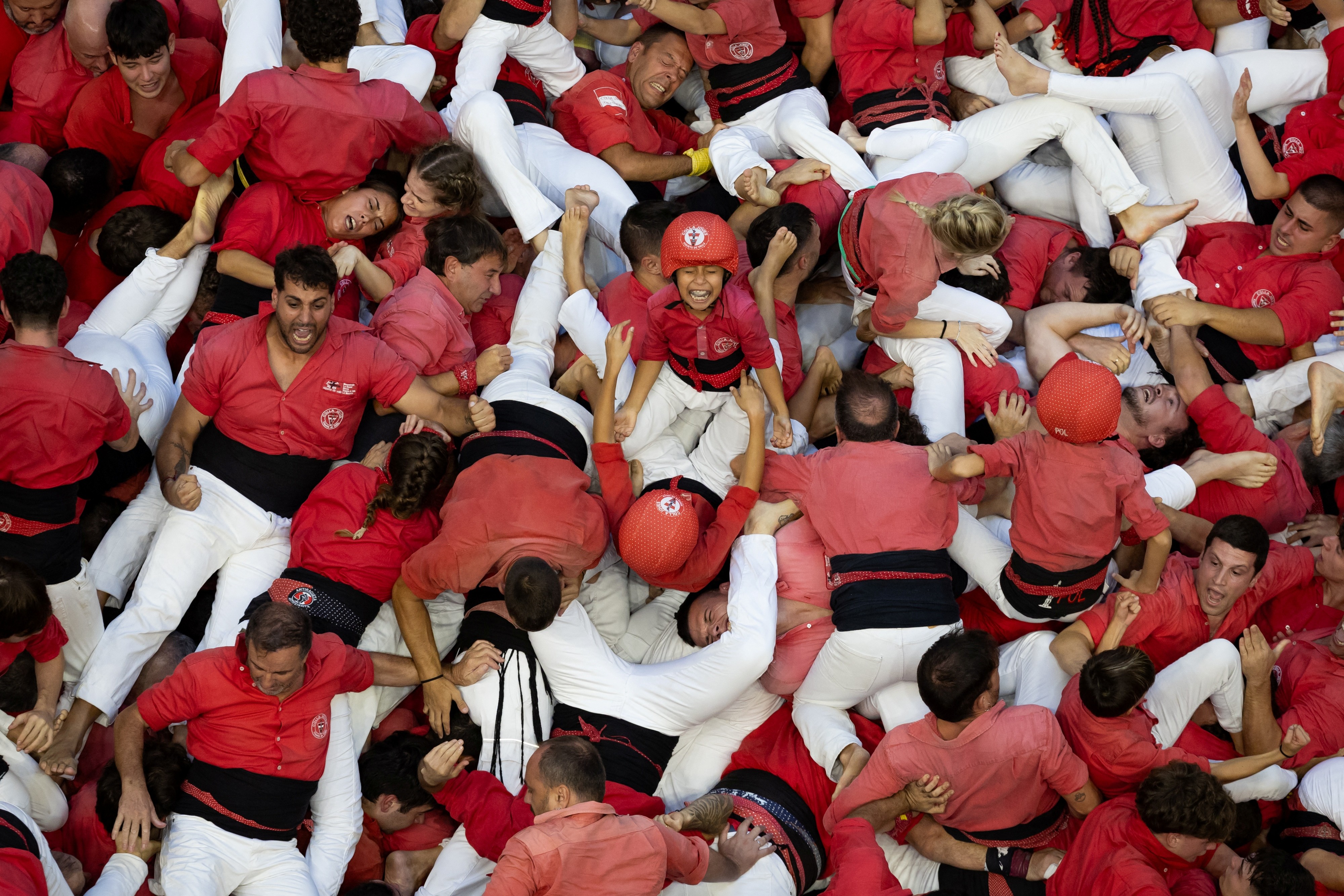 An overhead view of a team that just built a human tower, then collapsed on top of each other in a pile, smiling and struggling