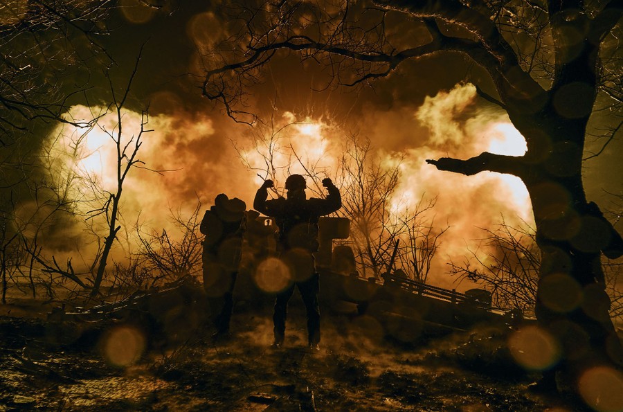 Ukrainian soldiers fire an artillery round at night, with flames spreading from the muzzle.
