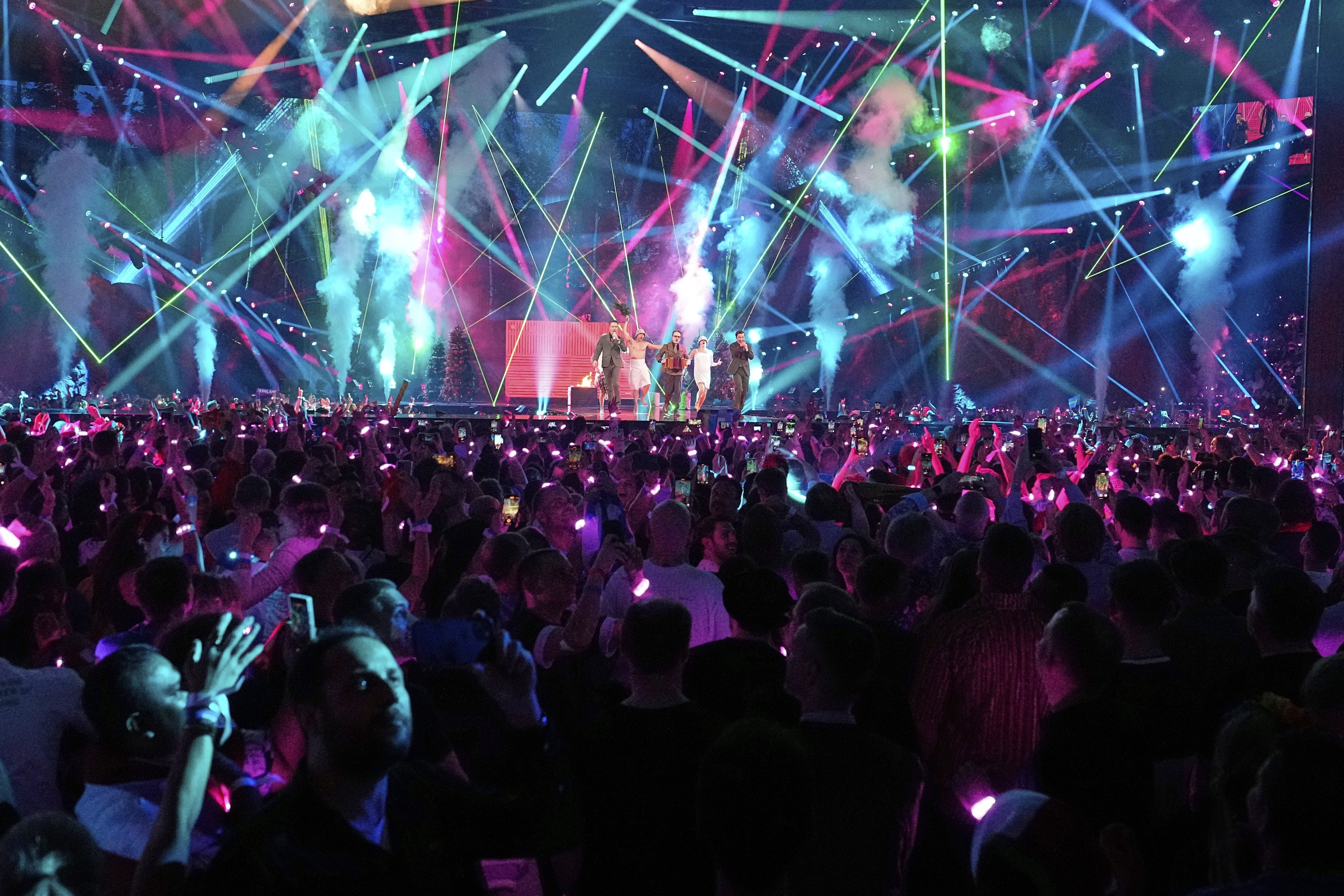 A group performed on the stage in front of a large crowd, and dozens of laser lights shining throughout the auditorium.
