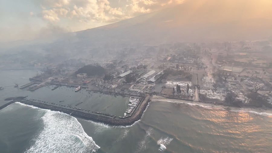 An aerial view of the coastline of a resort town, recently burned, with smoke still hanging in the air