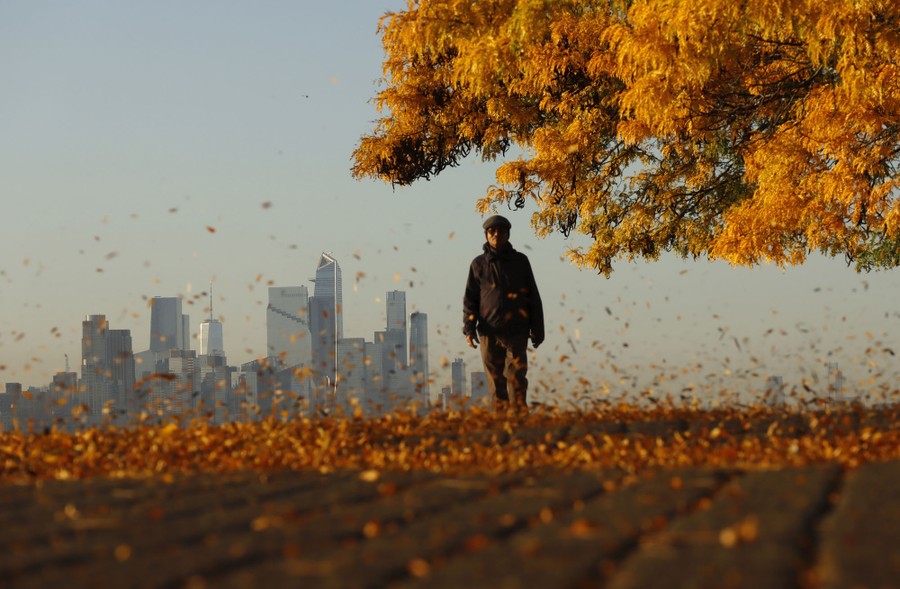 A person walks through blowing leaves in front of the New York City skyline.