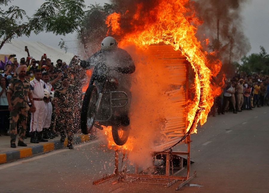 A motorcycle rider jumps through a flaming hoop in front of a crowd.