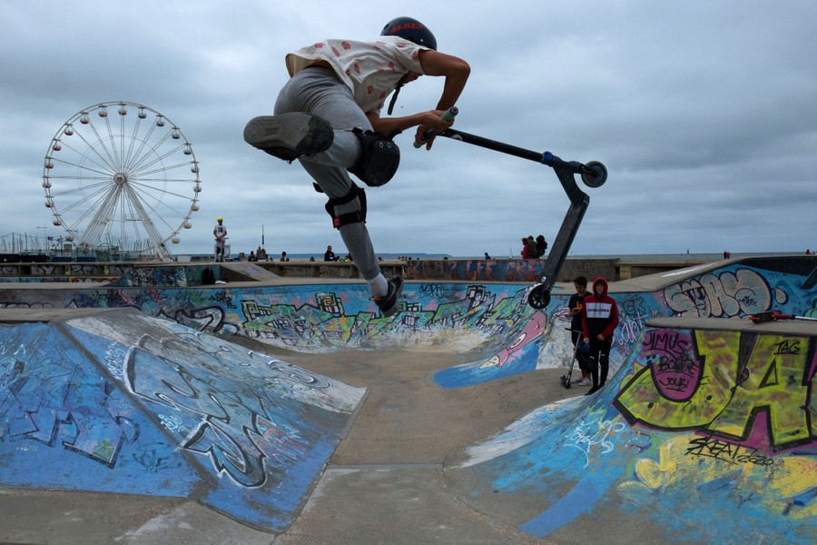 A person performs a trick with a scooter in a skate park.