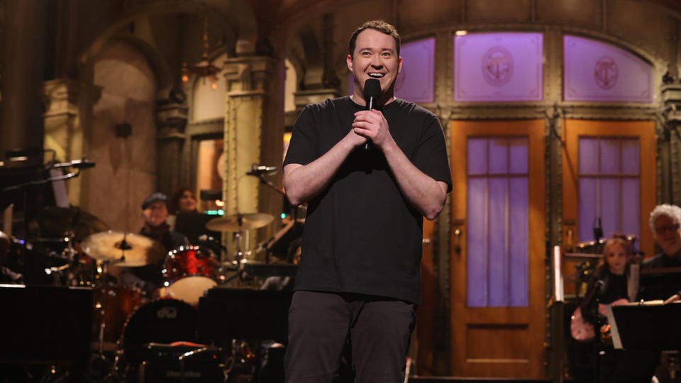 Shane Gillis holding a microphone and smiling onstage during "SNL"