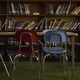 A red chair next to a blue chair in front of a desk and bookshelf