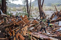 Search-and-rescue workers dig through debris alongside a recently flooded riverbed.