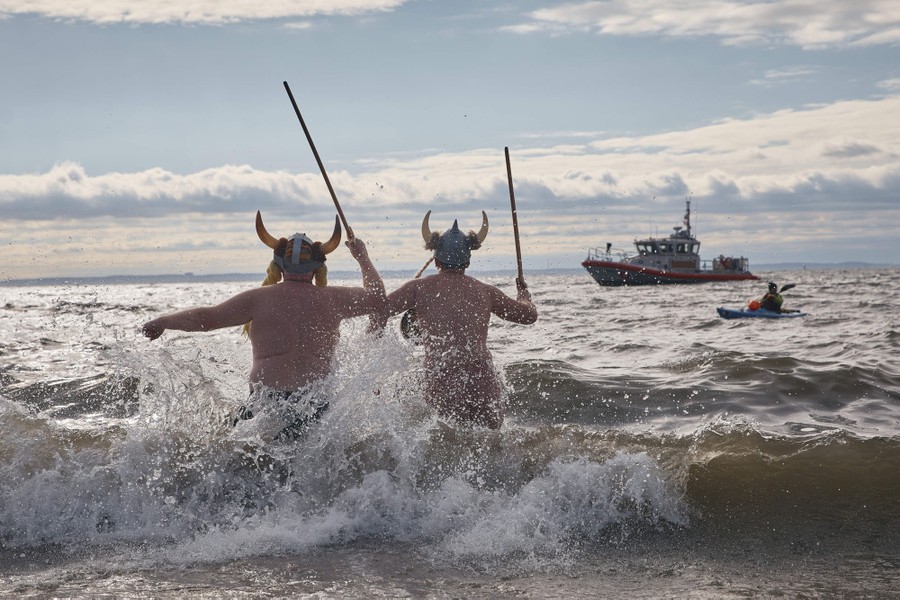 Two people wearing horned costume helmets run into the surf.