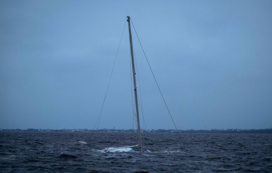 A sailboat lies partially submerged, only its mast above water.