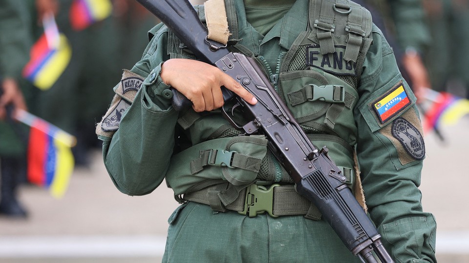 Color photograph of the torso of a Venezuelan soldier holding a gun downward across their body.