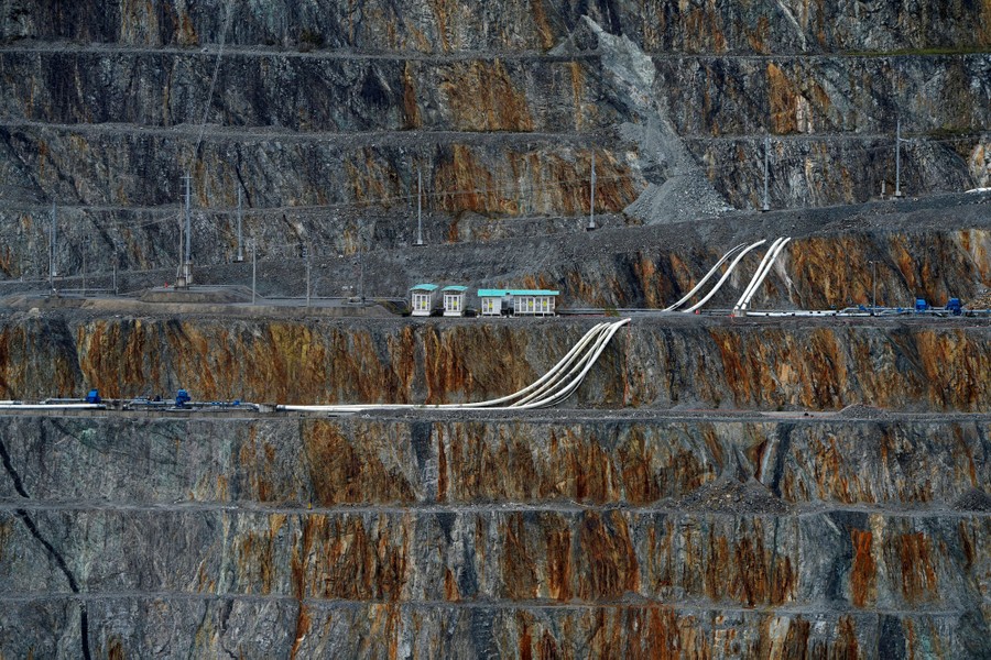 Several pipes are laid across sharp terraces along the side of a huge open-pit mine.