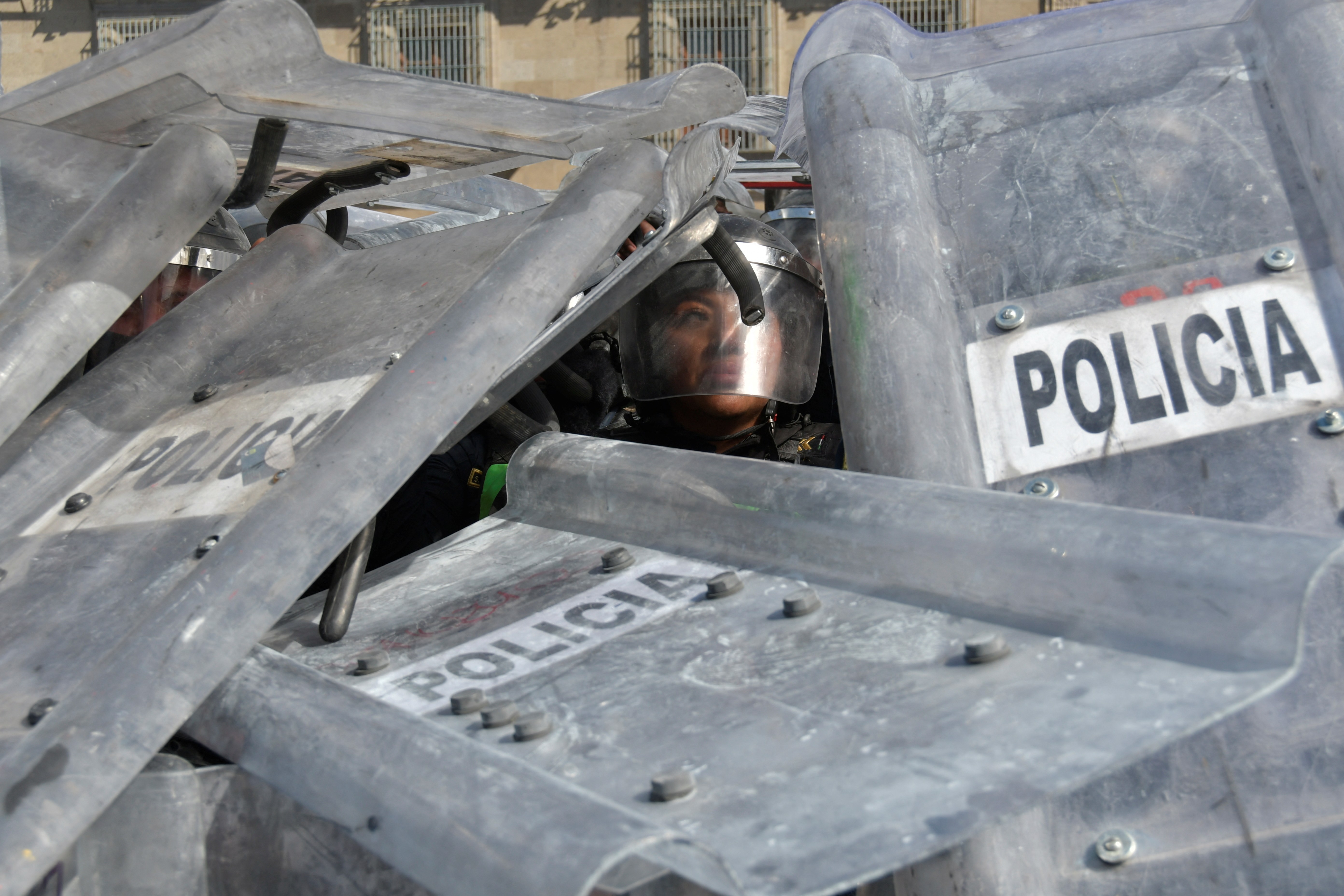 A cluster of riot police, covered in shields, with one police officer visible through a gap in the shields.