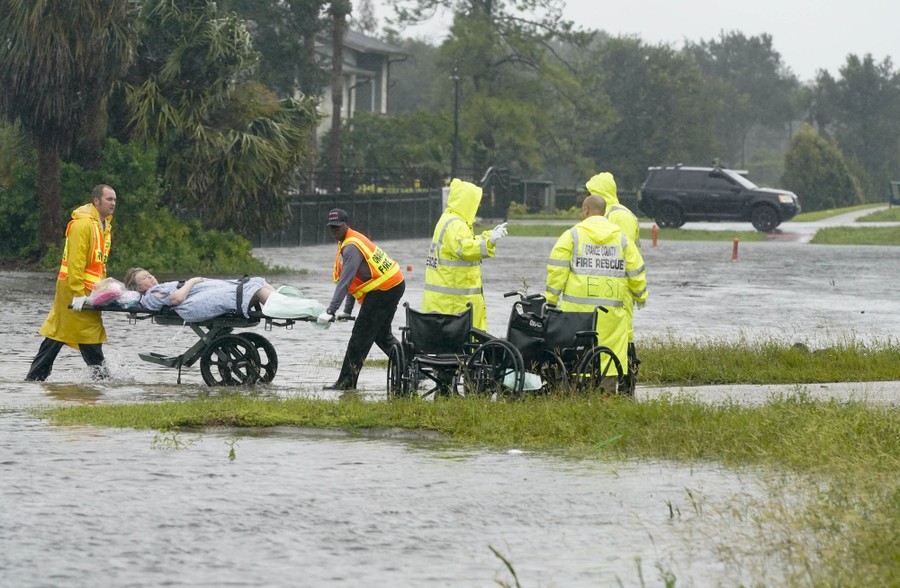 Emergency workers transport a person through a flooded area on a wheeled cart.