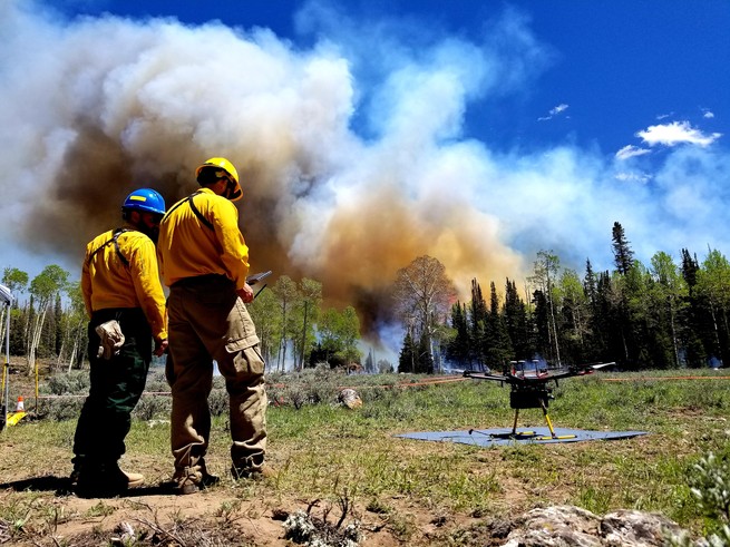 Two researchers stand beside a drone during a controlled burn.