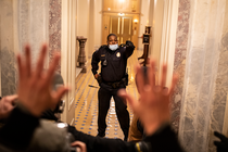 Photo of Capitol Police Officer Eugene Goodman standing in doorway of Capitol Building stairwell on January 6, 2021, with hand raised, opposite a crowd of rioters