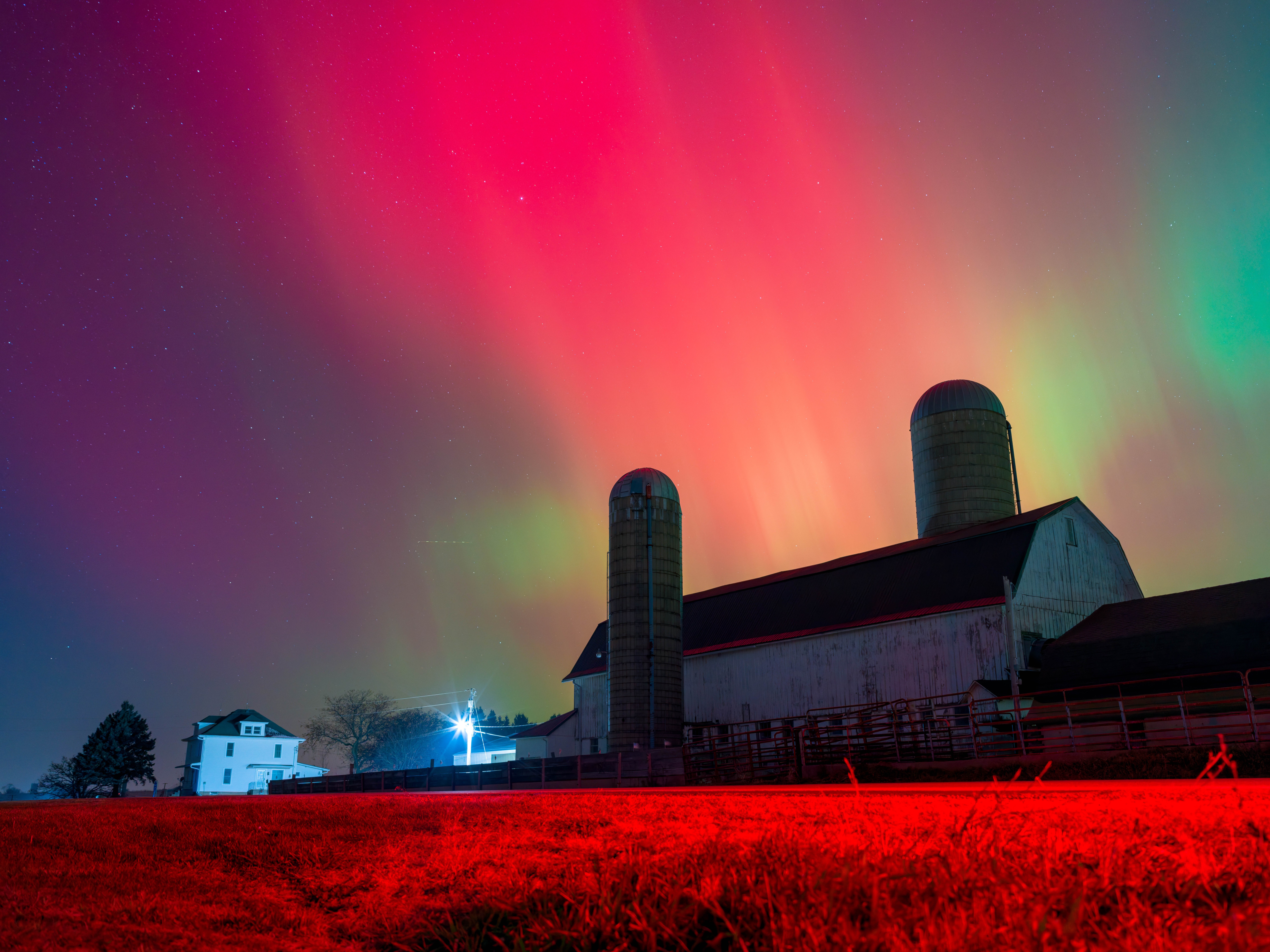 Sheets of red and green light glow in the night sky above a barn.