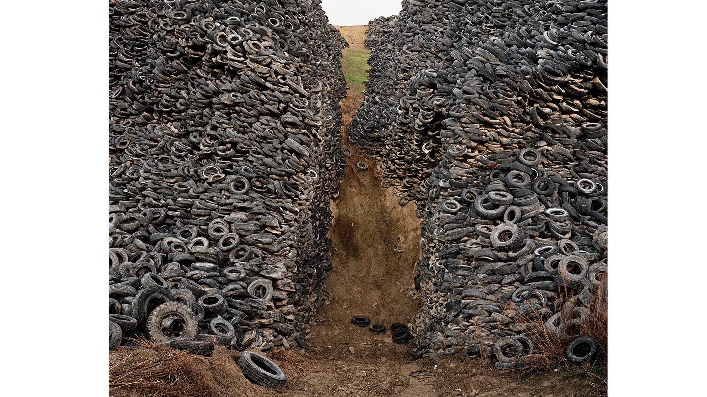 photo of enormous pile of discarded tires parted down the middle by dirt path with green hill just visible beyond