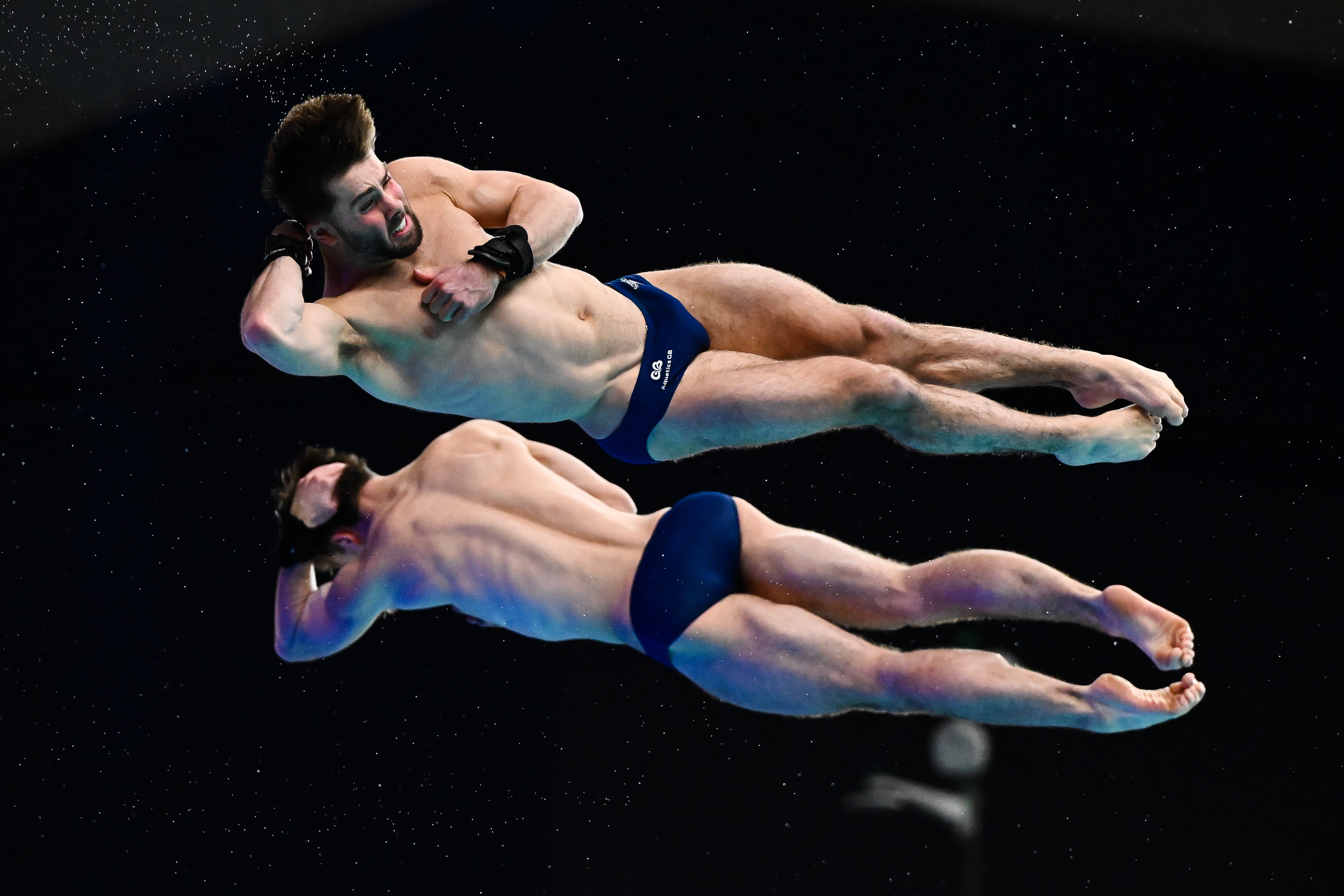Two divers, seen stretched out in the air, spinning, mid-dive.